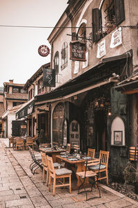 Empty chairs and tables at sidewalk cafe by buildings in city