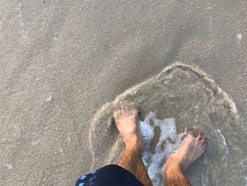 Low section of man standing on sandy beach