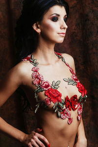 Shirtless young woman with floral decoration standing against wall