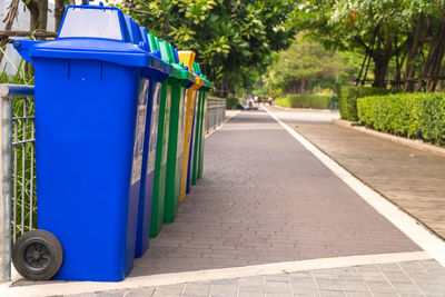 Colorful garbage cans arranged in row on footpath at park