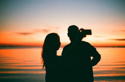 Silhouette people photographing sea against sky during sunset