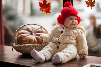 Cute baby girl in warm clothing sitting by pumpkin on table