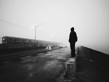 Full length of man standing on retaining wall at roadside in foggy weather