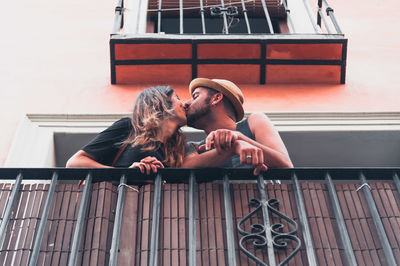Low angle view of young couple kissing at balcony