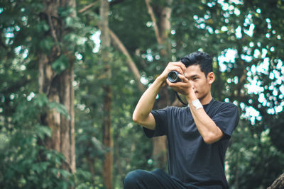 Young man photographing while sitting on tree