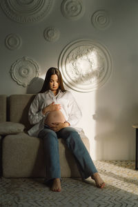 Cute young pregnant girl sitting on the white studio in warm light