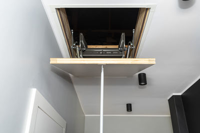 Folding metal stairs to the attic in the ceiling, closed hatch with a tube for opening, modern look.