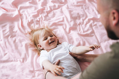 Happy father young man and baby girl little daughter having fun on bed in room at home