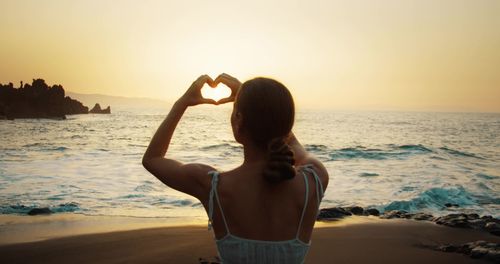 Rear view of woman with arms outstretched at beach during sunset