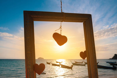 Close-up of wooden hanging over sea against sky during sunset