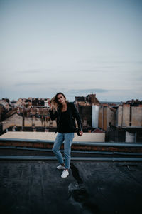 Portrait of happy young woman standing on building terrace against sky in city