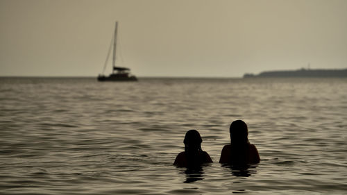 Silhouette women swimming in sea against sky during sunset