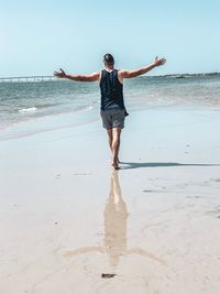 Rear view of man standing with arms outstretched at beach against sky