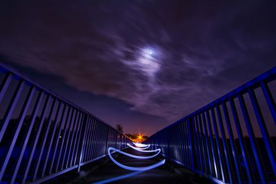 Light trails on bridge over lake against sky at night