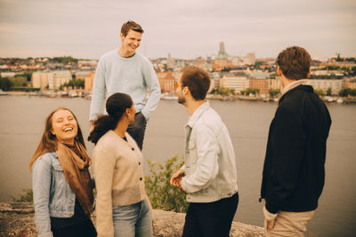 Happy friends standing against lake in city during picnic