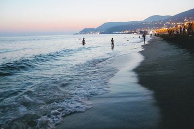 People on beach against sky during sunset