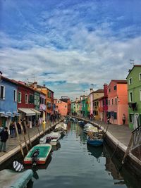 Boats moored in canal amidst buildings against sky