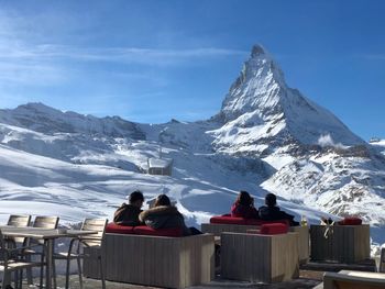 Rear view of people sitting on chair at restaurant against snowcapped mountain 