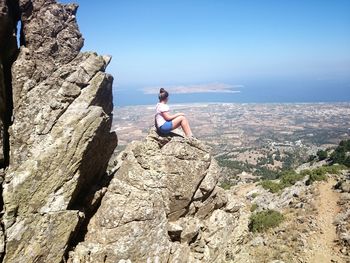 Woman sitting on rock formation against sky