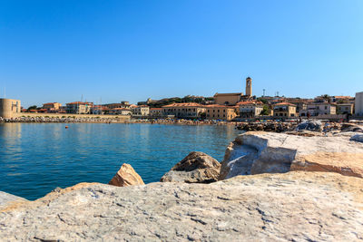 Buildings by sea against clear blue sky