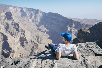 Rear view of man lying on cliff against sky