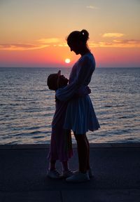 Mother embracing daughter while standing at beach against sky