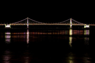 Illuminated bridge over river against sky at night