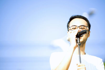 Close-up of man singing while standing against blue sky