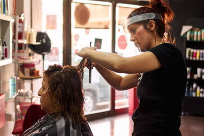 Hairdresser cuts a client's hair with a face shield