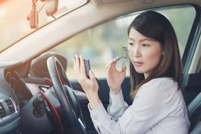 Young woman applying make-up in car