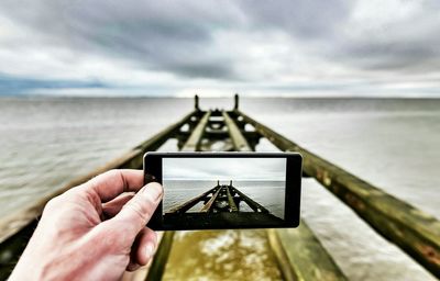 Person hand holding camera on beach against sky