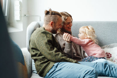 Smiling parents looking at daughter playing on sofa