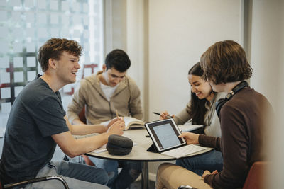 Happy young students discussing while studying at table together in university