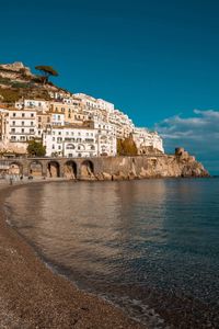 Buildings by sea against blue sky