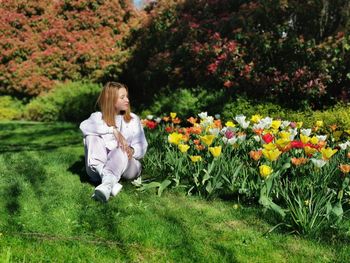 Full length of woman sitting by flowers on land