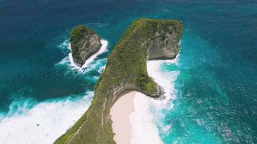 Best travel destination kelingking sandy beach with tall overgrown rocky cliff and turquoise ocean.