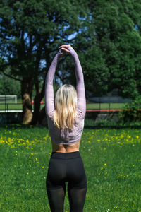 Young caucasian blond-haired woman in sportswear is doing yoga in public park. outdoor workout.