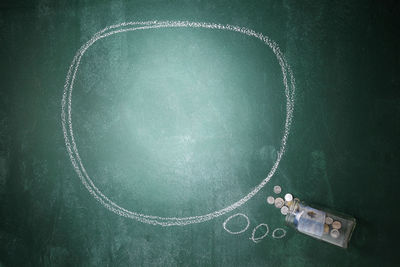 Directly above shot of blank speech bubble with currency in jar on blackboard