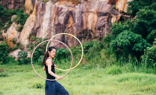 Side view of woman spinning hula hoop while walking on grassy field