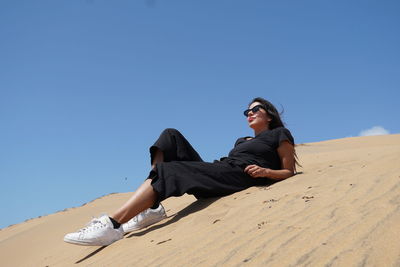 Young woman sitting on sand against clear sky