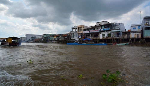 Buildings by river against sky in city