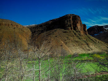 Low angle view of rocky mountain against clear blue sky