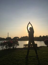 Silhouette man standing by lake against sky during sunset