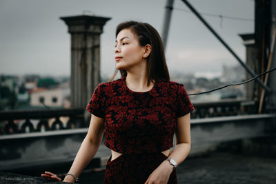 Young woman looking away while standing against sky