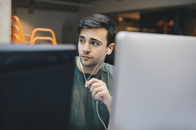 Thoughtful computer programmer wearing in-ear headphones in office