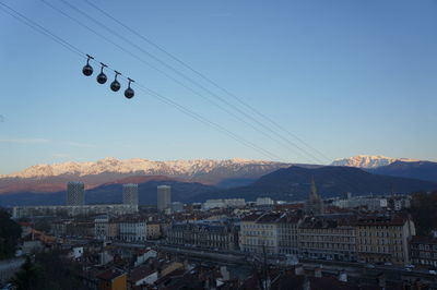 Overhead cables cars over cityscape against clear sky