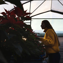 Side view of woman examining plants in greenhouse