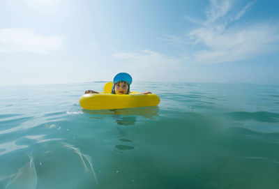 Portrait of boy sitting on pool raft at sea against sky