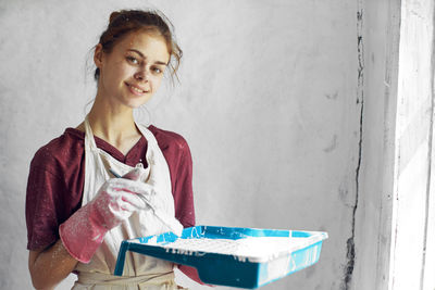 Young woman using digital tablet while standing against wall