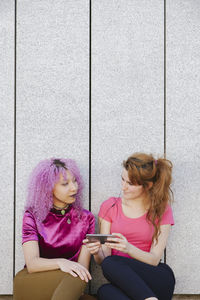 Lesbian couple looking at each other while sitting against wall